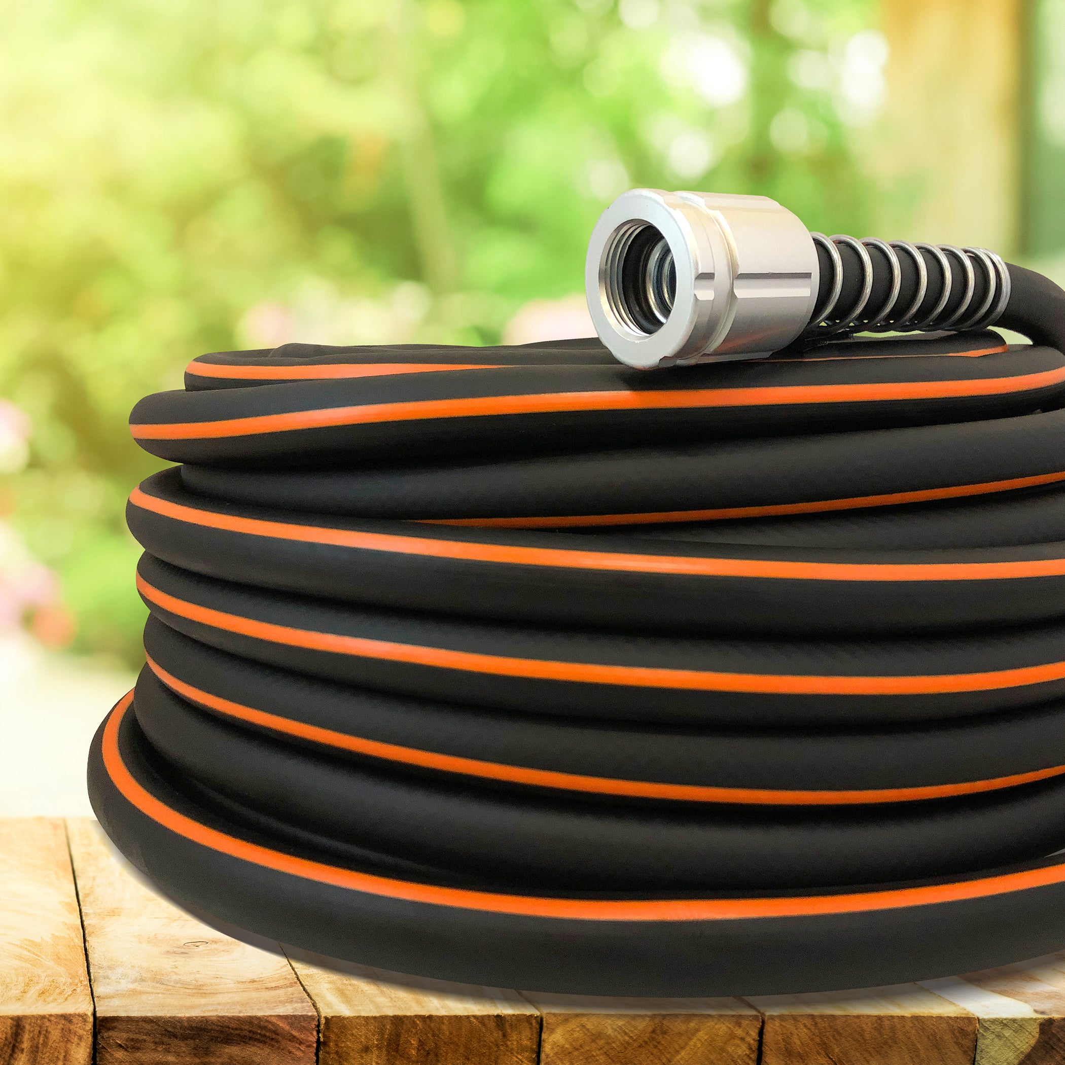 Coiled black garden hose with orange stripes and a silver nozzle on a wooden surface.