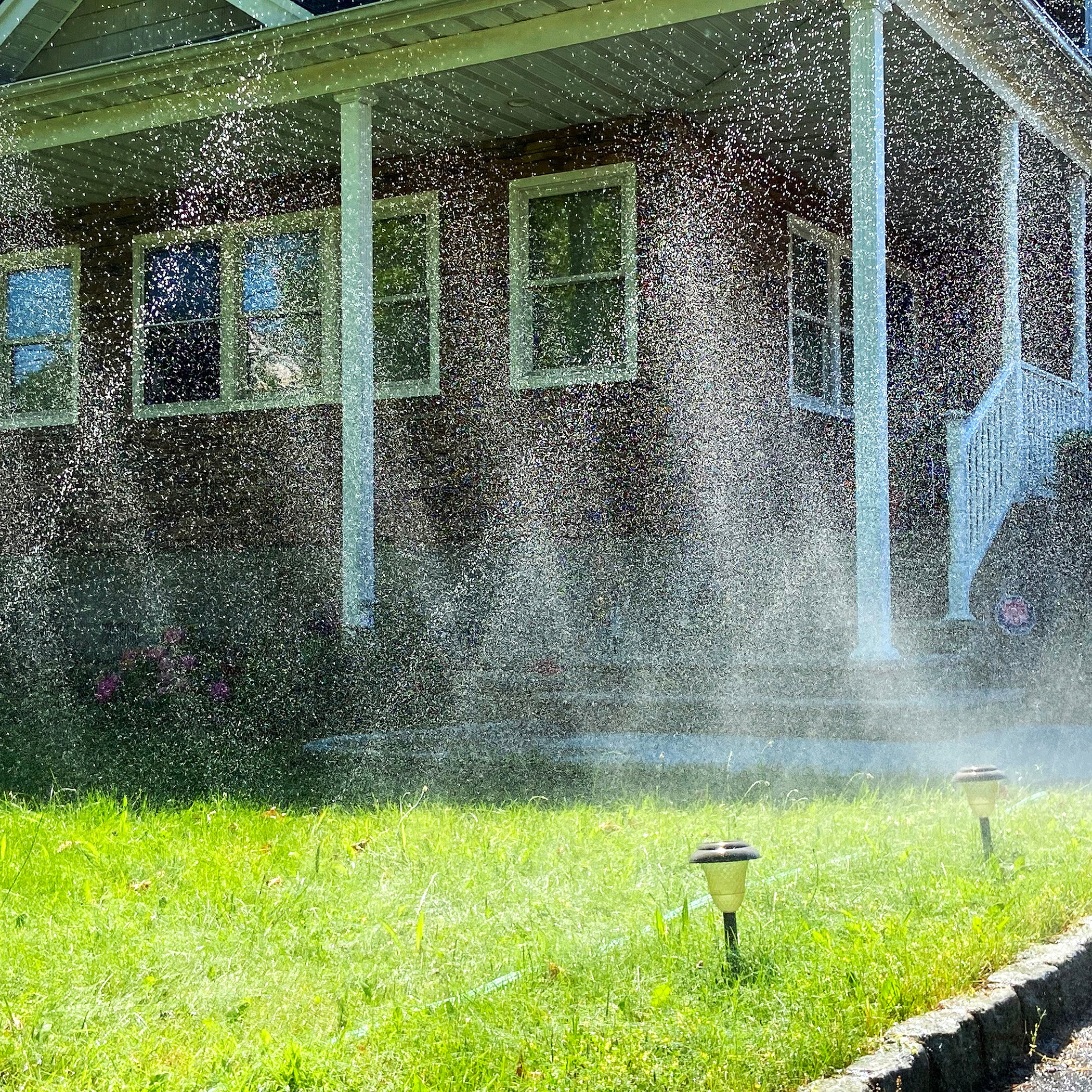 Sprinkler spraying water on a grassy area in front of a house