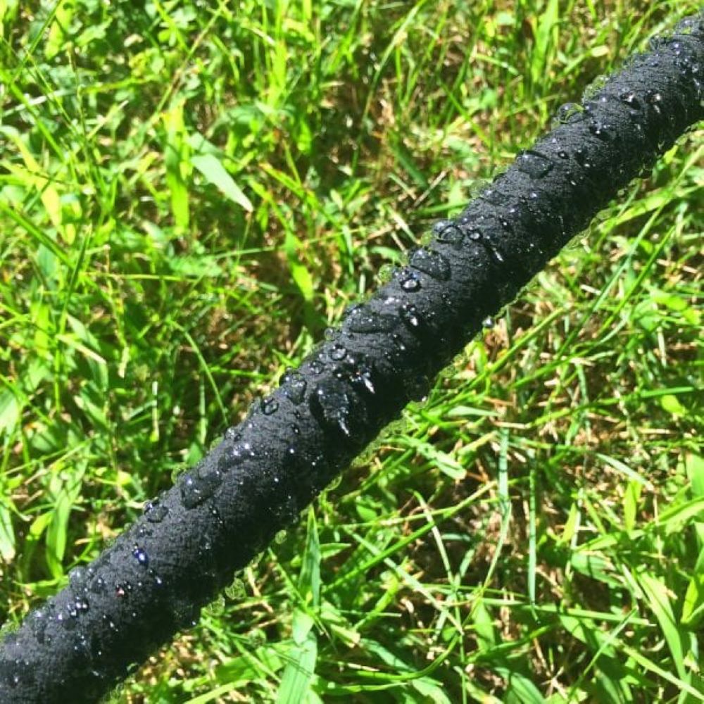 Black garden hose with water droplets on a grassy background